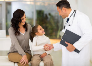 male doctor looking at the little girl with her mother smiling